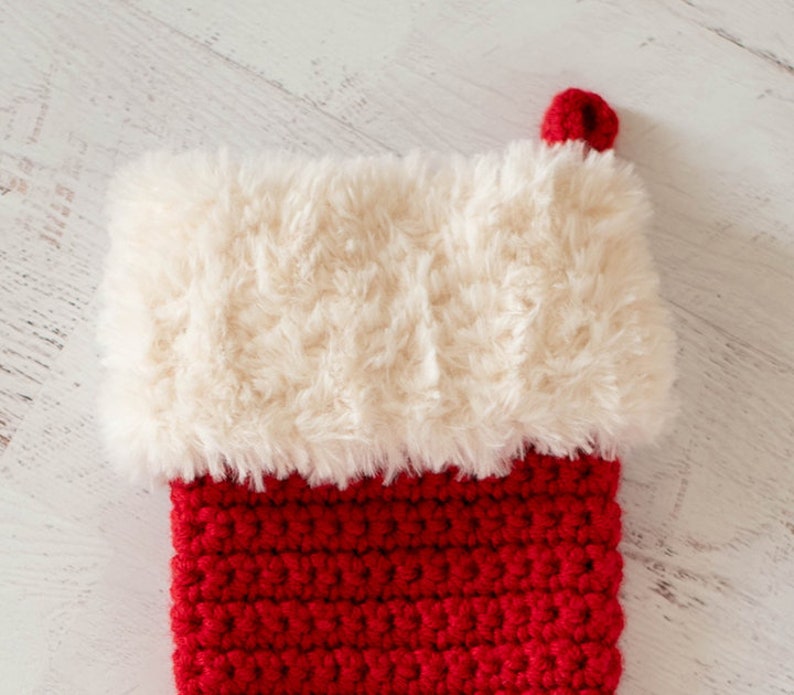 Puede incluir: Un calcet&iacute;n de Navidad de crochet rojo y blanco con un pu&ntilde;o blanco esponjoso.