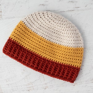 Può includere: Un berretto lavorato a uncinetto con tre strisce di colore: rosso, giallo e bianco.