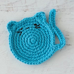 May include: A crocheted blue cat-shaped coaster with black embroidered whiskers.