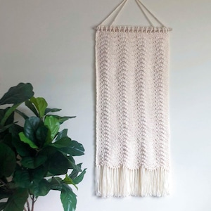 May include: A white crocheted wall hanging with a fringe border. The hanging is attached to a wooden dowel rod with a white cord.