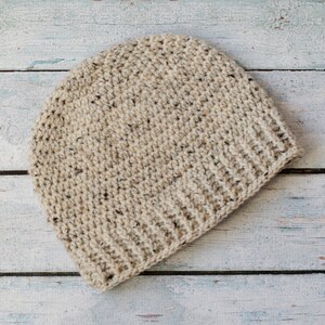 May include: A beige crocheted beanie hat with a textured pattern. The hat is made with a soft yarn and has a simple, classic design.