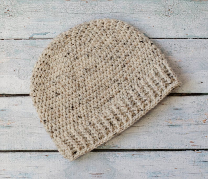 May include: A beige crocheted beanie hat with a textured pattern. The hat is made with a soft yarn and has a simple, classic design.