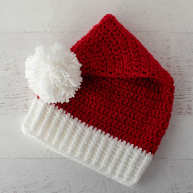 Op de afbeelding: Een rood-witte gebreide kerstmanmuts met een witte pompon bovenop.