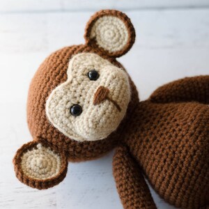 May include: A brown crocheted monkey toy with beige ears and a beige face. The monkey has black eyes and a small brown nose.