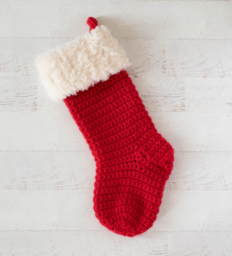 Puede incluir: Un calcet&iacute;n de Navidad rojo de ganchillo con un pu&ntilde;o de piel sint&eacute;tica blanca.
