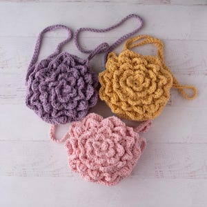 May include: Three round crochet bags with a textured floral petal design. One bag is purple, one is mustard yellow, and one is light pink. Each bag features a matching crocheted shoulder strap and a layered, dimensional surface pattern.