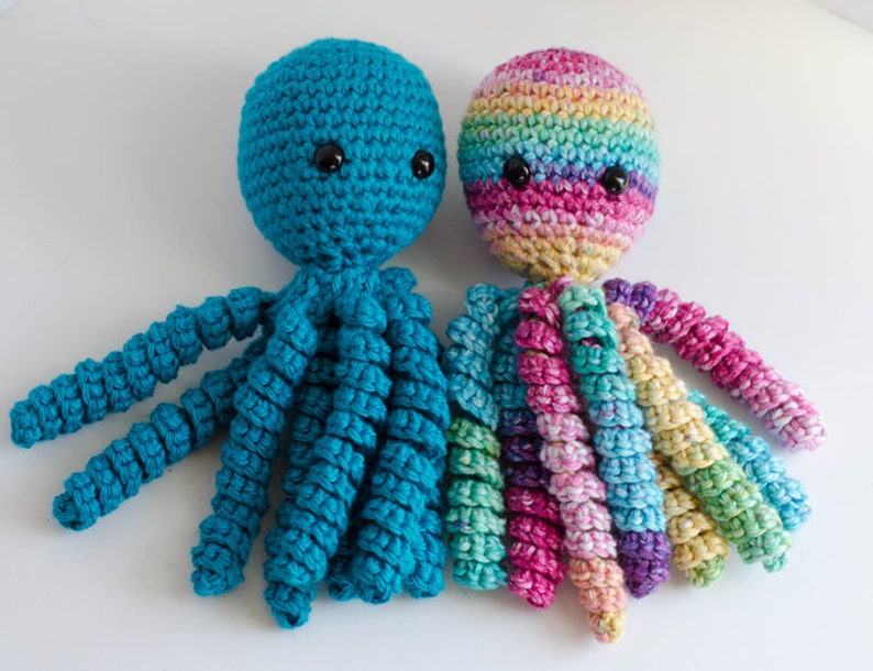 May include: Two crocheted octopus toys. One is teal blue, the other is multicolored with rainbow hues. Both have black button eyes and curled tentacles. These handmade plush toys are suitable for children.