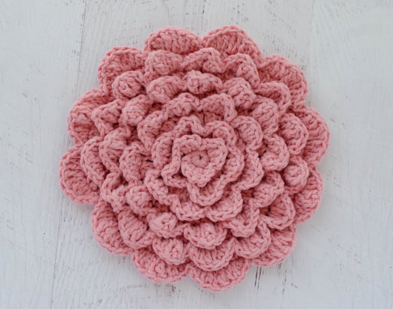 May include: A pink crocheted flower with a textured, layered design. The flower is made with a soft yarn and has a delicate, feminine look.