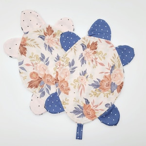 May include: Two turtle-shaped fabric items. The main body features a floral pattern with peach and brown flowers, blue leaves, and a cream background. The head and flippers are made of pink polka dot and blue polka dot fabric.