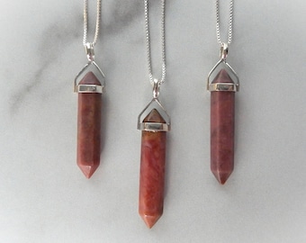 May include: Three silver necklaces with red and brown gemstone pendants in the shape of a point. The pendants are attached to silver chains.