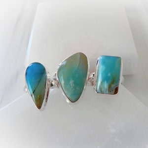 May include: Three silver rings with turquoise gemstones. The rings feature a teardrop, oval, and rectangular shaped stone.
