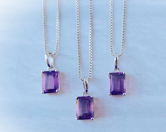 May include: Three silver necklaces with purple amethyst gemstone pendants. Each pendant is a rectangular cut gemstone.