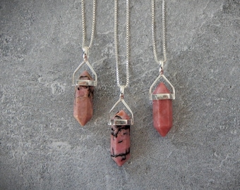May include: Four silver necklaces with pink and black crystal point pendants. The necklaces are on a gray background.