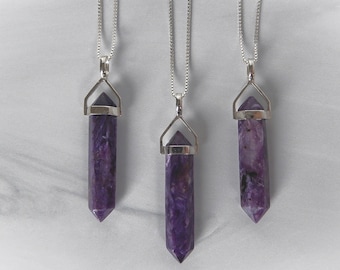 May include: Three silver necklaces with purple crystal pendants. The pendants are shaped like points and have a silver cap at the top.