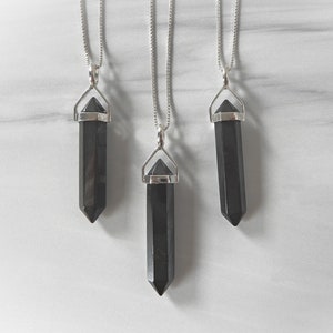 May include: Three silver necklaces with black crystal pendants in the shape of a point. The pendants are all the same size and shape, and they are hanging from silver chains.