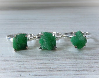 May include: Three silver rings with green gemstone settings. The gemstones are rough and have a natural, unpolished look.