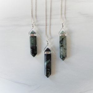 Puede incluir: Tres collares de cadena plateada con colgantes de cristal de punta verde y negro. Los colgantes tienen todos la misma forma y tamaño, pero diferentes patrones.