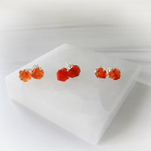 May include: Three pairs of carnelian earrings with silver posts. The carnelian stones are a deep orange color and have a natural, rough texture.