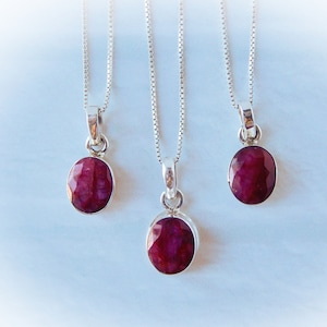 Könnte beinhalten: Drei silberne Halsketten mit roten Edelstein-Anhängern. Die Anhänger sind oval geformt und haben eine facettierte Oberfläche.