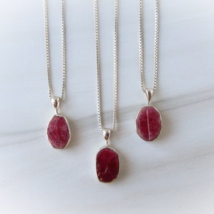 Puede incluir: Tres collares de cadena de plata con colgantes de rubí rojo. Los colgantes son todos de diferentes formas y tamaños.