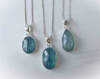 May include: Three silver necklaces with aquamarine gemstone pendants. The pendants are different shapes, including oval and teardrop.
