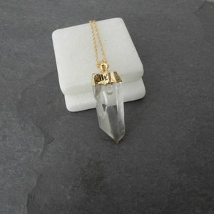 Puede incluir: Un collar de cadena dorada con un colgante de cristal de cuarzo transparente. El colgante est&aacute; engastado en un bisel dorado y tiene una punta puntiaguda.