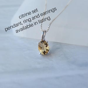Peut inclure: Un collier en argent avec un pendentif en forme de citrine ovale de couleur brun clair. Le texte "citrine set pendant, ring and earrings available in listing" est visible sur l'image.