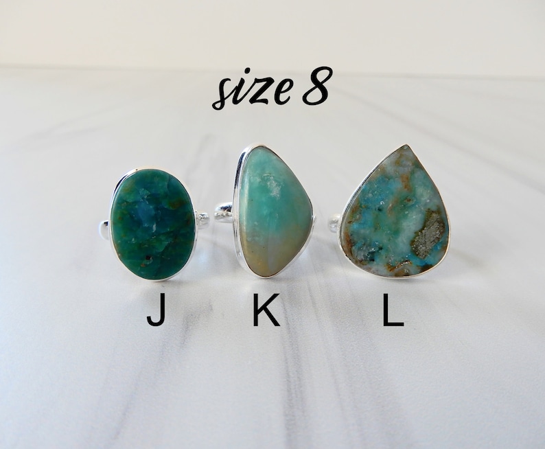 May include: Three silver rings with different shaped turquoise stones. The rings are labeled J, K, and L. The text "size 8" is above the rings.