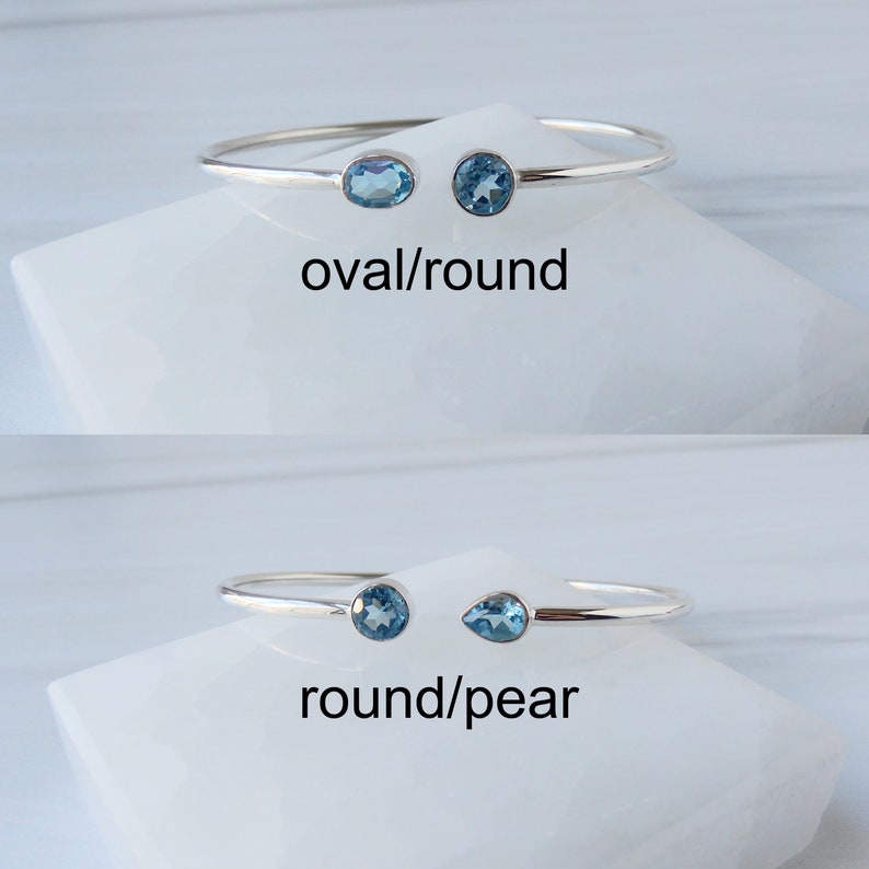 May include: Two silver bangle bracelets with blue gemstones. The top bracelet has an oval and round gemstone. The bottom bracelet has a round and pear-shaped gemstone. The text "oval/round" and "round/pear" is below each bracelet.