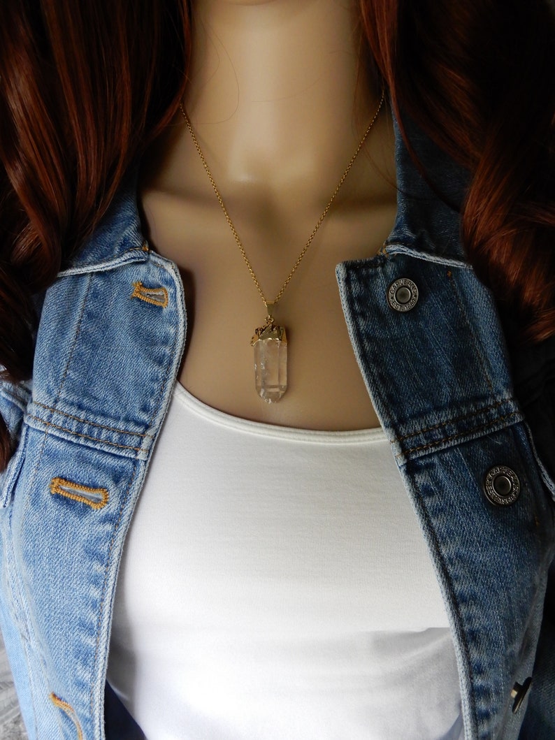 Puede incluir: Un collar de cadena dorada con un colgante de cristal de cuarzo transparente. El colgante est&aacute; facetado y tiene un engaste dorado.