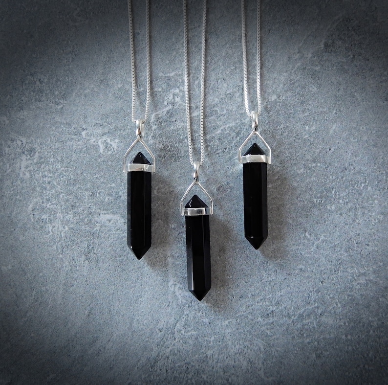 May include: Three silver necklaces with black crystal point pendants. The pendants are all the same shape and size, and they are hanging from silver chains.