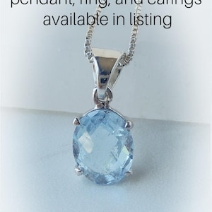 May include: A silver chain necklace with a pendant featuring a light blue topaz gemstone. The text "blue topaz set pendant, ring, and earrings available in listing" is visible above the necklace.