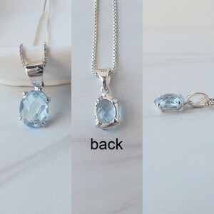 May include: A silver chain necklace with a light blue oval gemstone pendant. The pendant is set in a silver bezel and has a 925 stamp on the back.
