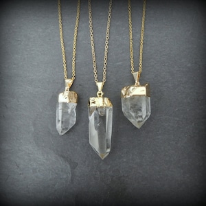 Puede incluir: Tres collares de oro con colgantes de cristal de cuarzo transparente. Los colgantes son de diferentes tama&ntilde;os y formas. Los collares est&aacute;n sobre un fondo gris.