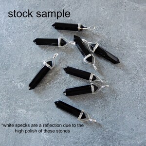 May include: A group of seven black obsidian crystal point pendants with silver bail settings. The pendants are arranged on a gray surface. *white specks are a reflection due to the high polish of these stones*