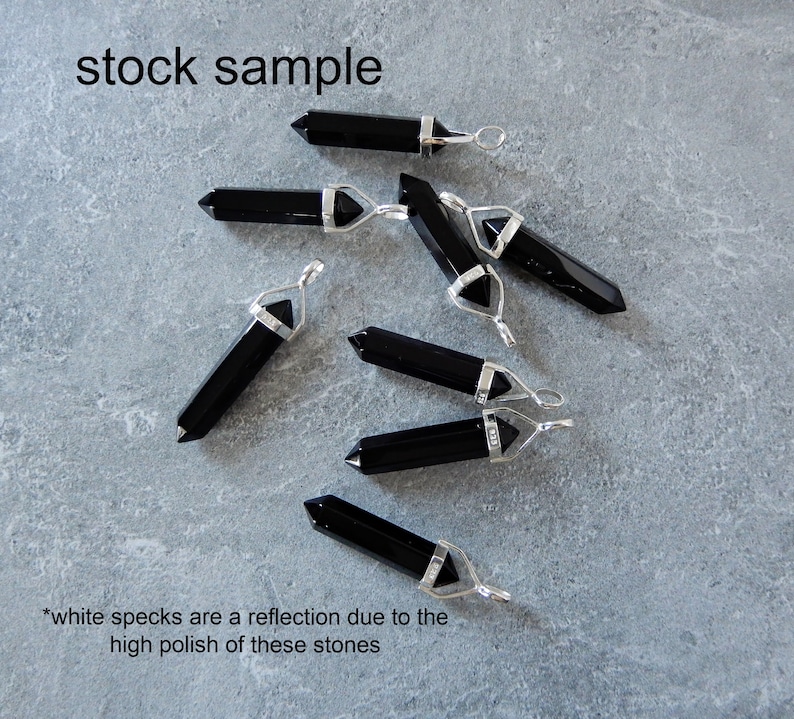 May include: A group of seven black obsidian crystal point pendants with silver bail settings. The pendants are arranged on a gray surface. *white specks are a reflection due to the high polish of these stones*