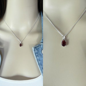 Pu&ograve; includere: Una collana con catena d'argento con un piccolo ciondolo di forma ovale con una pietra rossa.
