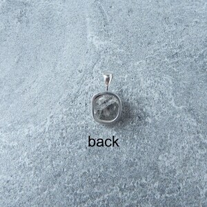 May include: Silver pendant featuring a clear, faceted gemstone. The back of the pendant is visible, showing the bail.
