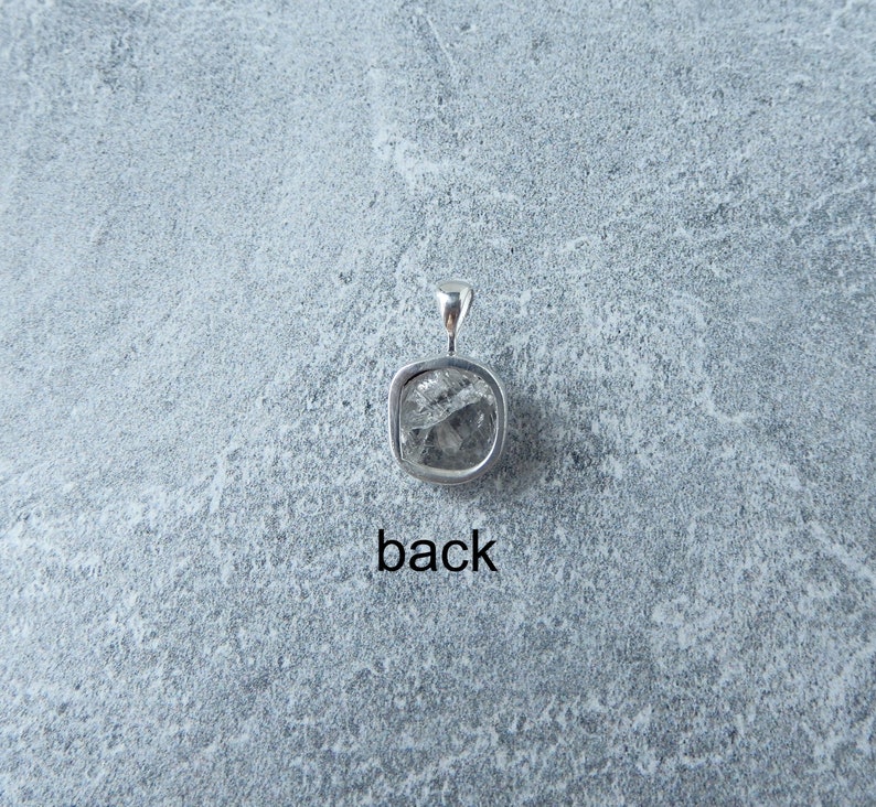 May include: Silver pendant featuring a clear, faceted gemstone. The back of the pendant is visible, showing the bail.