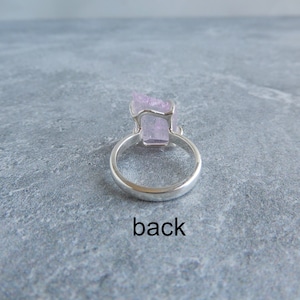 K&ouml;nnte beinhalten: Ein silberner Ring mit einem rosafarbenen Kristall in der Mitte. Die R&uuml;ckseite des Rings ist auf dem Bild zu sehen. Der Ring liegt auf einer grauen Oberfl&auml;che. Das Wort "back" steht unter dem Ring.