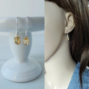 Peut inclure: Une paire de boucles d'oreilles pendantes en argent avec des pierres pr&eacute;cieuses en topaze de forme ovale. Les boucles d'oreilles sont pr&eacute;sent&eacute;es sur un pi&eacute;destal blanc et sur l'oreille d'un mannequin.
