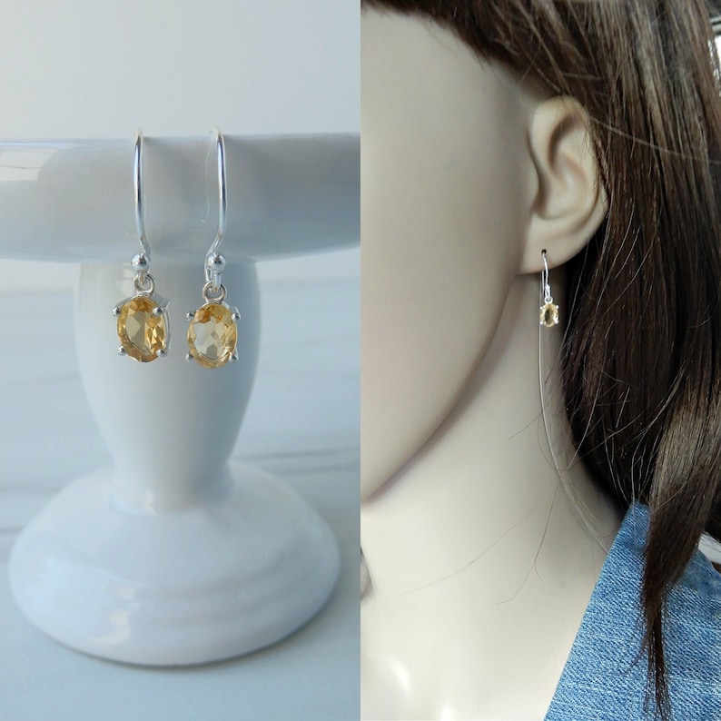 Peut inclure: Une paire de boucles d'oreilles pendantes en argent avec des pierres pr&eacute;cieuses en topaze de forme ovale. Les boucles d'oreilles sont pr&eacute;sent&eacute;es sur un pi&eacute;destal blanc et sur l'oreille d'un mannequin.