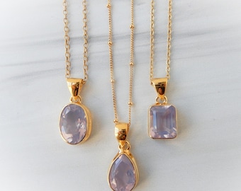 May include: Three gold-tone necklaces featuring light purple, translucent, faceted gemstone pendants. The left pendant is oval, the center is teardrop-shaped on a beaded chain, and the right is rectangular. Each pendant is set in a gold-tone metal frame.
