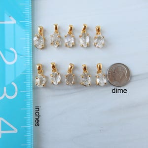 May include: Ten gold pendants with clear, irregular-shaped stones are shown. A dime is next to the pendants for size comparison. A blue ruler with inch markings is on the left side of the image.