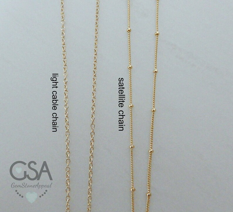 Puede incluir: Dos cadenas de oro, una es una cadena de cable ligero y la otra es una cadena de sat&eacute;lite. Las cadenas cuelgan sobre un fondo blanco.