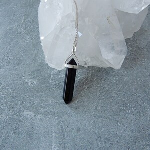 May include: A black crystal point pendant on a silver chain. The pendant is hanging from a piece of white quartz.