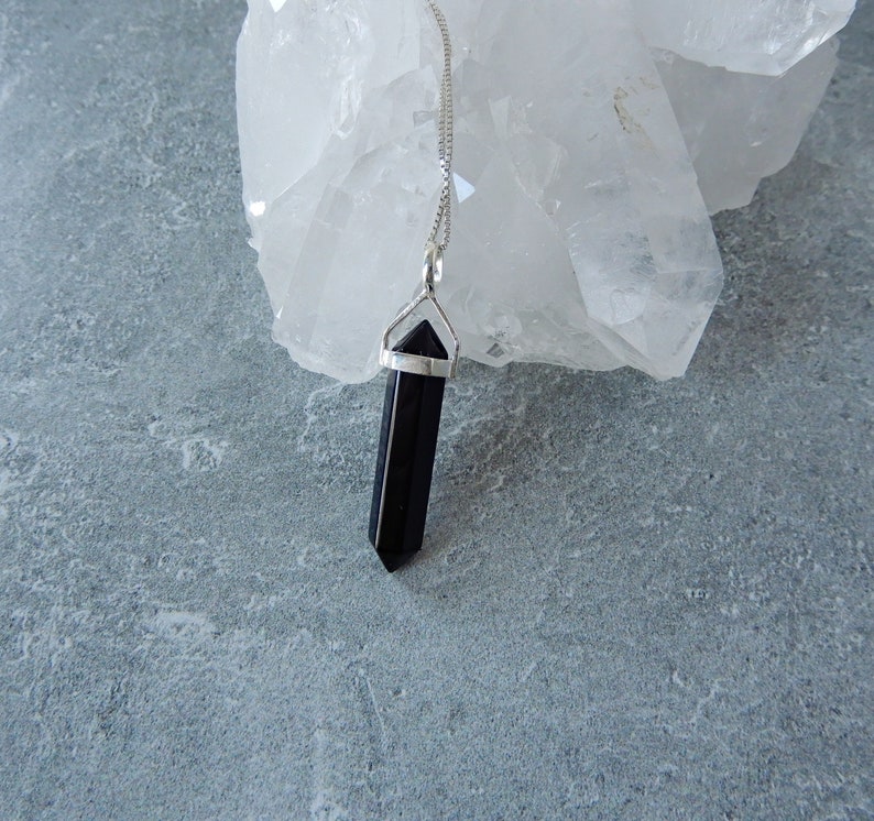 May include: A black crystal point pendant on a silver chain. The pendant is hanging from a piece of white quartz.