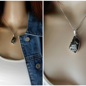 May include: A silver chain necklace with a raw, black, natural stone pendant. The pendant is a rough, irregular shape.