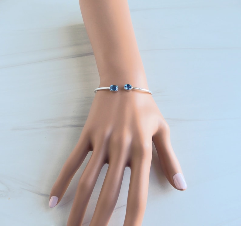 May include: A silver bangle bracelet with two blue gemstone accents.