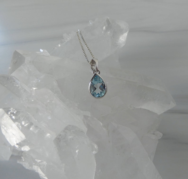 May include: A teardrop-shaped blue topaz pendant necklace on a silver chain. The pendant is set in a silver bezel and is surrounded by clear quartz crystals.